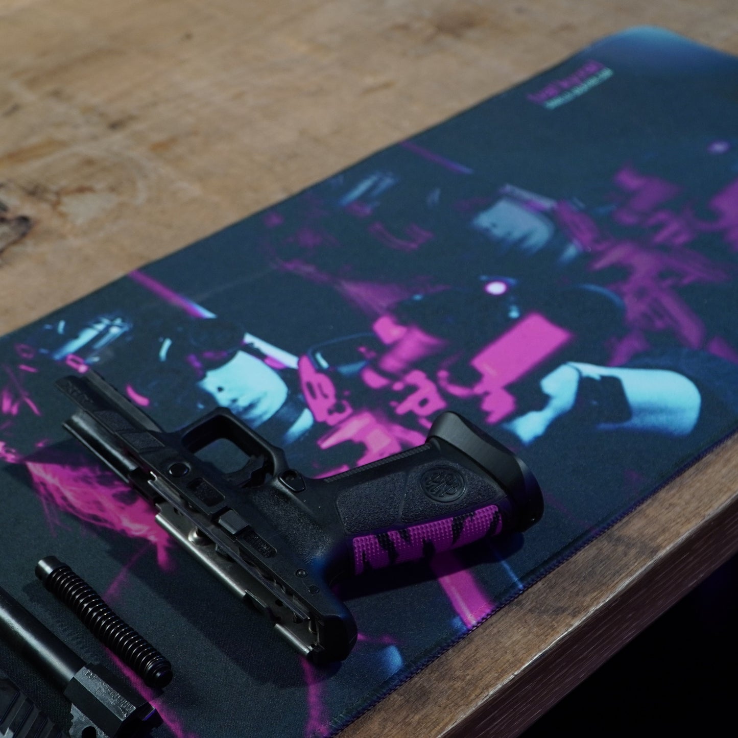 Black gun parts on a colorful mouse pad with a wooden surface underneath